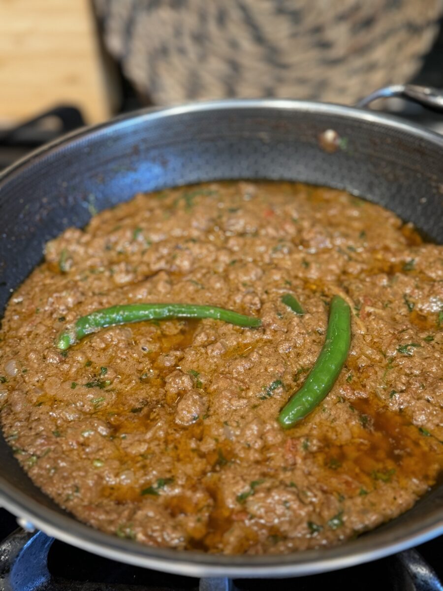 Bhuna Qeema served in a karahi with roti and garnished with ginger and green chilies
