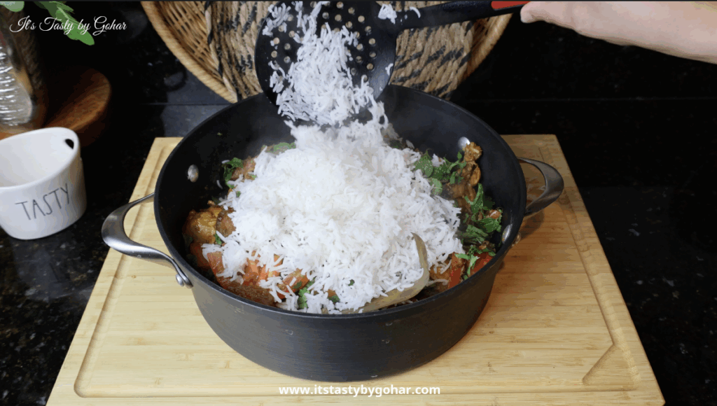 Layering biryani rice over chicken korma with fried onions and mint